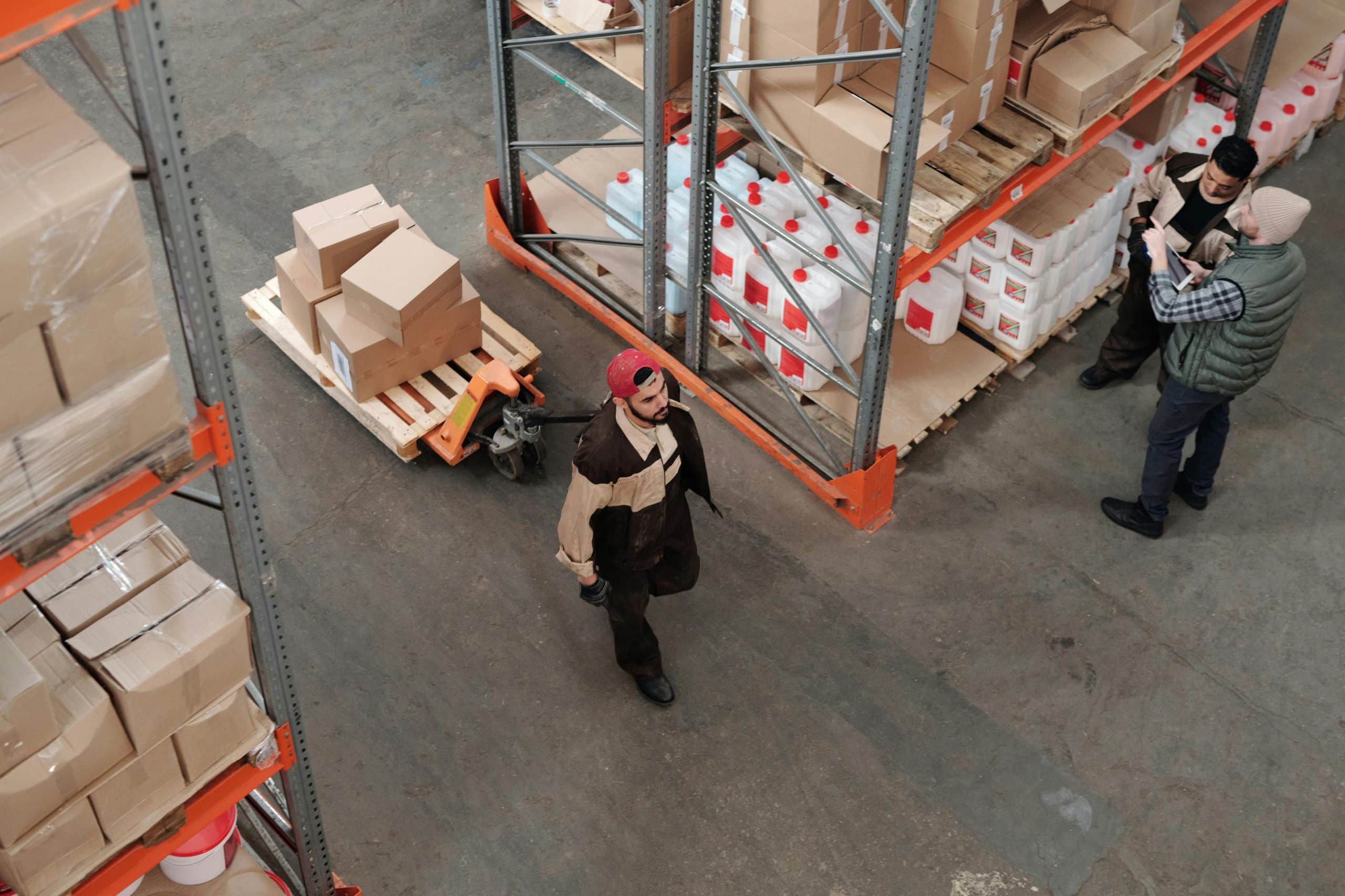 Un magazzino con del personale che sta lavorando, un operatore trasporta merce, altri verificano la merce sugli scaffali